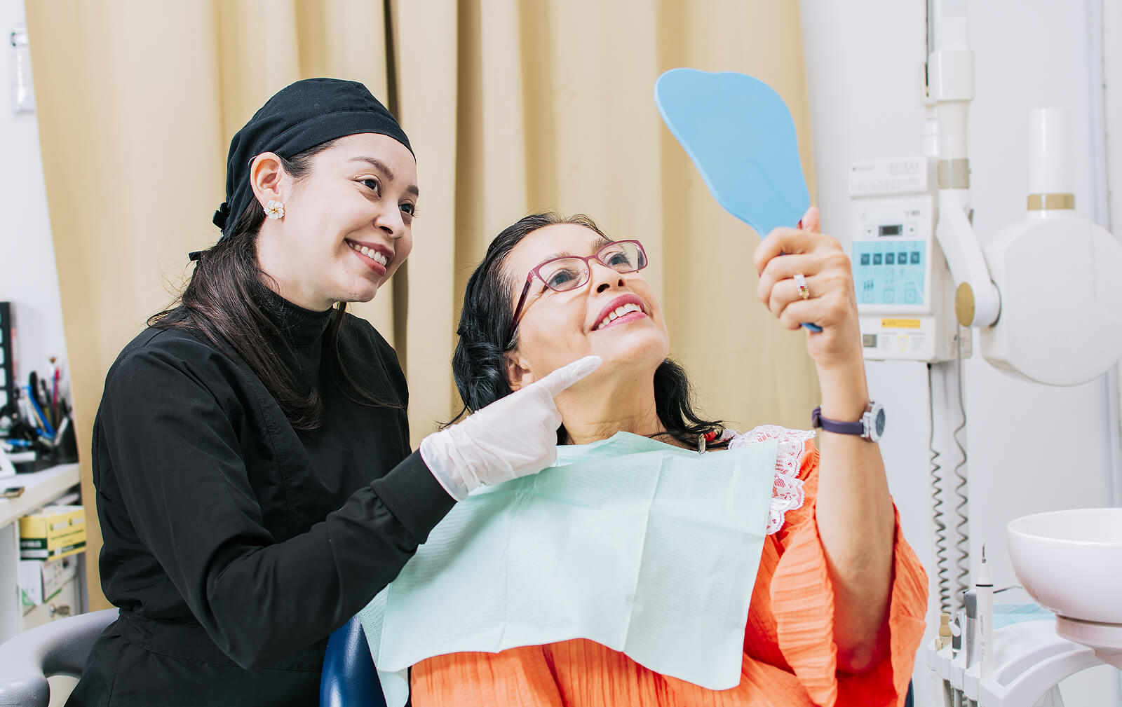 a patient looking at newly cleaned teeth in mirror with hygienist