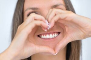 a woman making a heart with her hands and framing her perfect smile