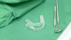 Picture of two Invisalign aligners sitting next to dental instruments on a green cloth.