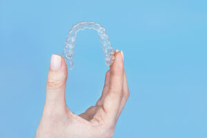 Picture of a person holding an Invisalign aligner in front of a light blue background.