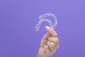 Picture of a person holding two Invisalign aligners in front of a purple background.
