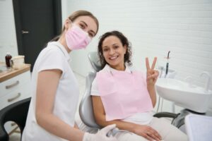 a happy patient giving a peace sign while smiling with a dental hygienist