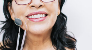 Picture of a woman smiling with two dental teeth cleaning instruments next to her face.