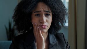 a woman in business attire holding her cheek due to a tooth ache
