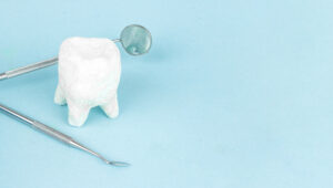 Picture of a white tooth figure and two dental instruments against a blue background.