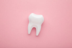 Picture of a white tooth figure in front of a pink background.
