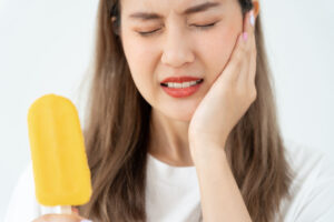 Picture of a woman holding her face in pain while eating a popsicle because she needs a root canal.